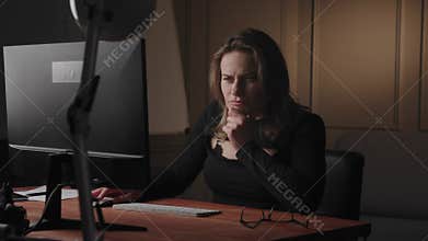 A young serious and thoughtful European or American blonde businesswoman or freelancer sits at the workplace, works in