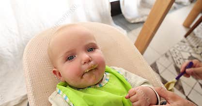 Six-month-old baby reaches out to the camera while being fed vegetable puree