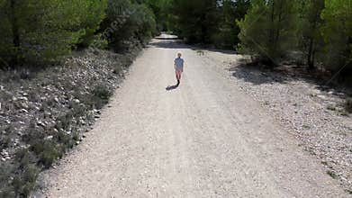 Drone shooting from the sky, a blond boy walks along a mountain road.