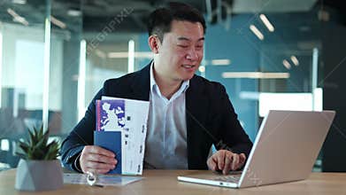 Travel adviser holding tickets and booking hotel on laptop while sitting at desk