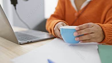A young woman enjoys a coffee break while working on a laptop and podcasting in a modern studio