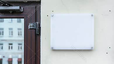 Blank white signboard on wall with screws, mockup for logo or text. Clear signage on textured wall beside wooden door