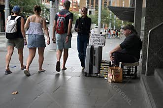 Young adult Australian people pass by an Australian panhandler adult man
