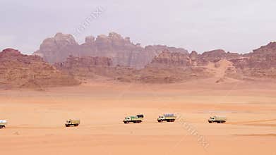 Convoy of supply trucks crossing Wadi rum desert with sandstone mountains remote logistics support transport production concept