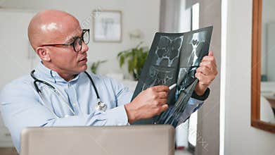 Bald Doctor in Glasses Explaining X-Ray Scan During a Telemedicine Consultation on Laptop
