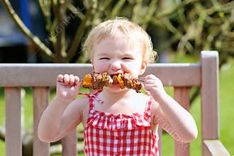 Funny little girl eating grilled meat from spoon