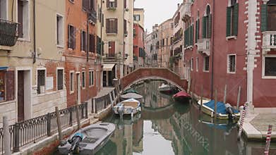 Narrow Venetian Canal with Arched Bridge and Moored Boats in Venice Italy