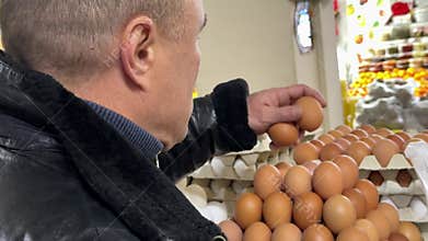 Man holds box of chicken eggs in hand examining integrity of shell before buying them in supermarket.