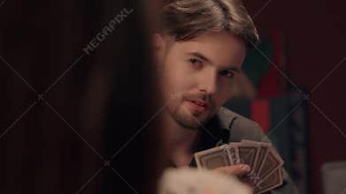 Focused Caucasian man gambler holding poker cards smoking cigar looking at rival at home casino thoughtful male guy