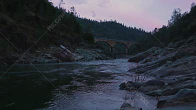Twilight River with Historic Arched Bridge and Rocky Shore
