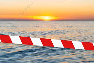 Barrier tape - quarantine, isolation concept, entry ban. Do not cross. Bright sunset with a yellow sun above the sea surface