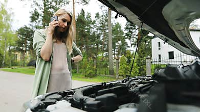 Assistance on the road - woman looking at broken car engine and talking on the phone