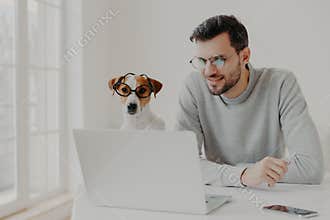 Busy man works freelance, watches training video online on laptop computer wears transparent glasses works together with jack