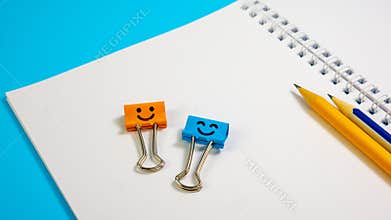 Blue and Orange Color Smile Binder Clips with Pencils on Paper Notepad
