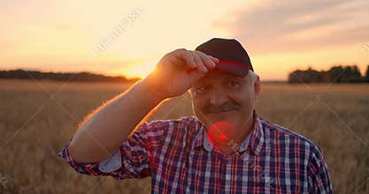 Portrait of a smiling Senior adult farmer in a cap in a field of cereals. In the sunset light, an elderly man in a