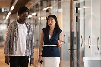 Two serious diverse colleagues talking walking in modern office hallway
