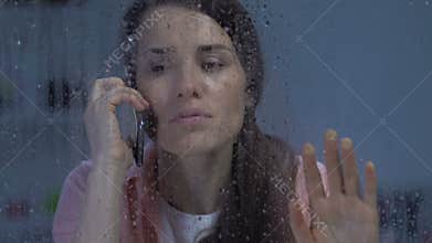 Upset female talking on phone, receiving bad news on rainy day, depression