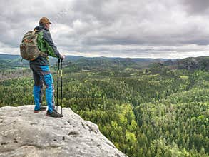 Man with a backpack and running shoes stands on top of a rock