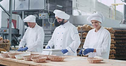 Very charismatic baker woman with a large smile and her colleagues bakers men forming the dough to baking the bread