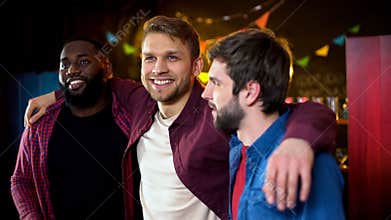 Cheerful multiracial friends hugging, celebrating bachelor party in bar, leisure