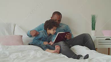 Joyful diverse family reading a book lying on bed