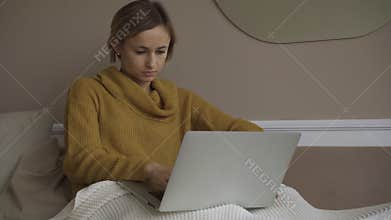 Student using laptop at home lying on sofa under blanket using computer serching for online consultation. People and