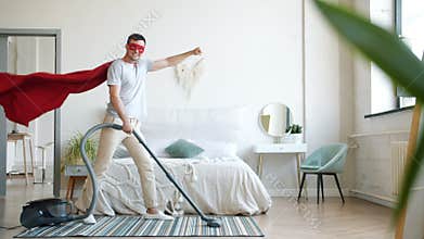 Portrait of smiling superman vacuuming carpet at home and looking at camera