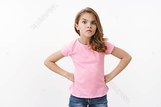 Serious-looking strict and angry little arrogant girl, blond child, stand in bossy offended pose, hold hands waist