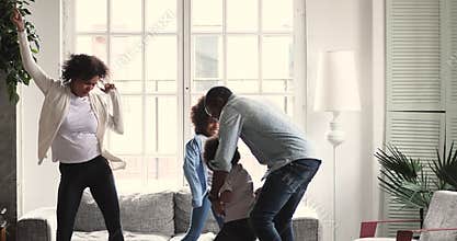 Happy african couple dancing with preschool children in living room