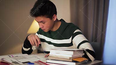 Side view close-up of tired Asian college student doing homework at home. Young handsome boy reading and writing in