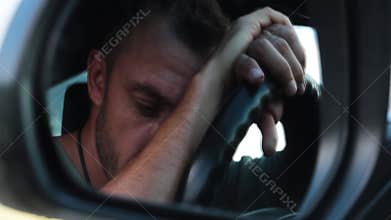 The man put his head on the steering wheel. Reflection in the mirror. A close-up.