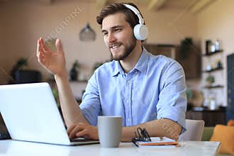 Happy young man in earphones working on laptop from home during self isolation