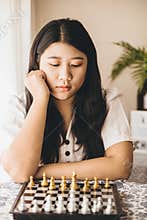 Smart girl teen thinking while playing Chess boardgame at home for training her brain and memory