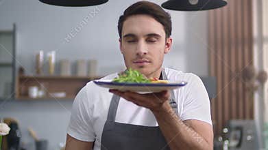 Man cook smelling salad at home kitchen. Cheerful chef presenting healthy food