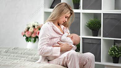 Smiling mother nursing cute toddler sitting on bed in cozy white bedroom. Medium shot on RED camera