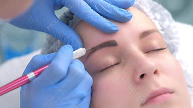 Beautician painting contour using manual tool for tattoo, woman`s face closeup.