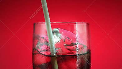 Drinking soft drink in glass with ice cube on red background. Cola or refreshment.