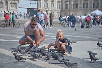 Father and daughter play with birds in Piazza Duomo in Milano