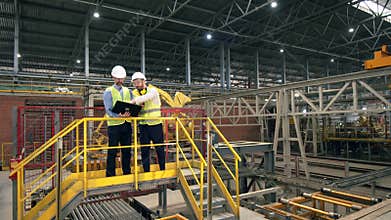 Two men work at a brick factory, checking machines. Professional factory workers at factory facility.