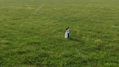 A couple of lovers stands in the middle of a field with green grass. They laugh, dance, kiss and inhale the aroma of