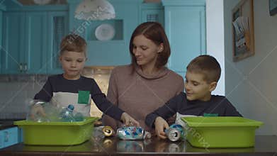 Young mother helping sons to sorting home garbage for recycling plastic and tin. Eco friendly family reducing plastic