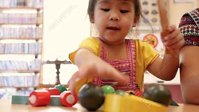 Cute little child girl having fun playing with cooking toys in living room at class room. Kid using wood toy knife slicing vegetab