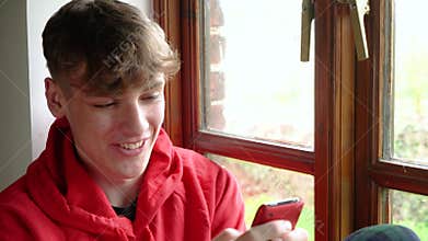 Teen male teenager young man adult wearing a red hoodie using mobile cell phone for texting or social media