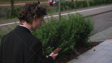 Back view successful businessman walking with phone at street. Confident man using smartphone outdoors. Serious business