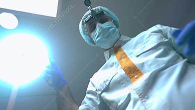 Bottom angle view of professional Middle Eastern dentist turning on dental lamp looking down at camera. Patient POV of