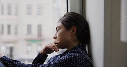 Upset Indian woman sits on windowsill staring out window
