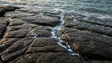 Coastal Black Rocks Interacting with Ocean Waves in Serene Seascape Under Bright Sunlight