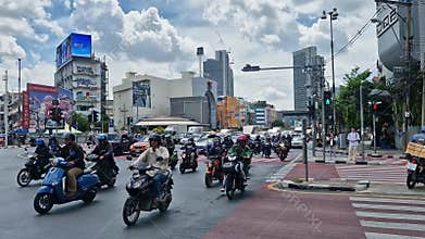 Bangkok, Thailand - 05082025 - A row of scooters and motorbikes exiting an intersection in the busy traffic of Bangkok, Thailand