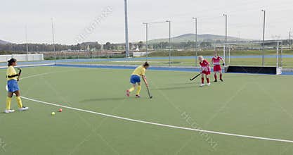 Female hockey players competing intensely on outdoor field, focusing on teamwork