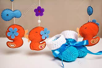 Blue knitted baby shoes with a blue ribbon around toys rattles.